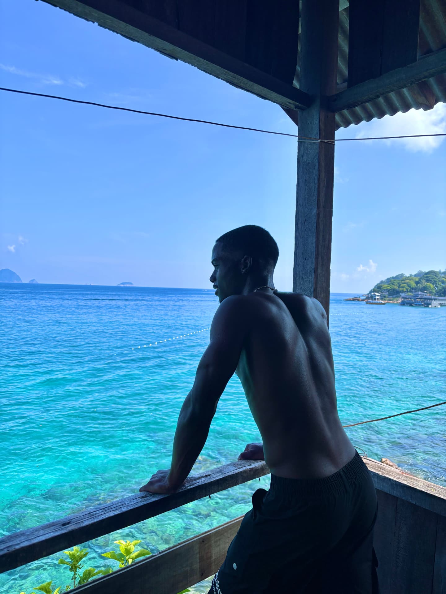 Leaning on a wooden balcony rail above clear turquoise water on a tropical island